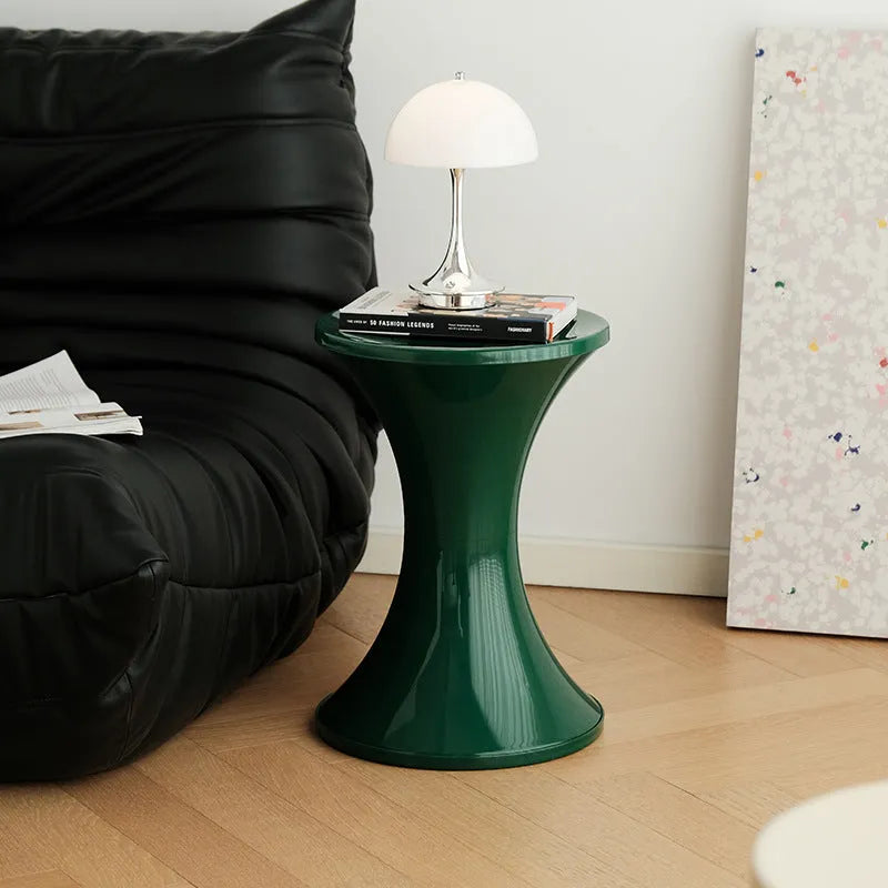 A green plastic hourglass-shaped shoe changing stool on a wooden floor.