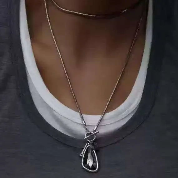 Geometric plaid pendant on a long snake chain necklace layered over a jumper.