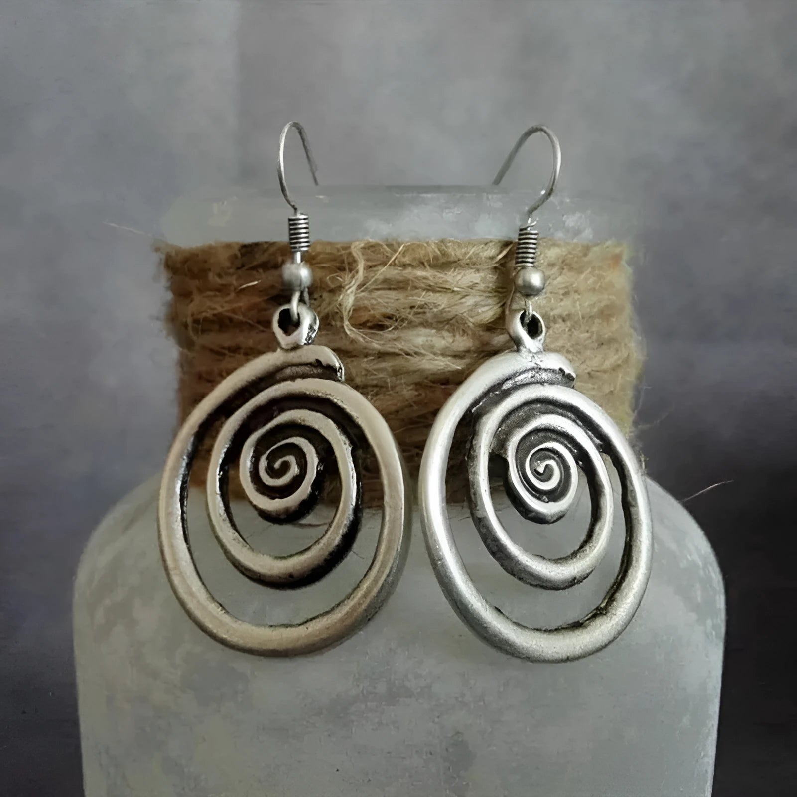 Close-up of a pair of silver geometric spiral earrings with a distressed vintage finish.