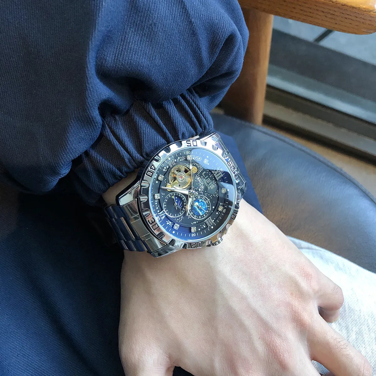 Men's silver automatic watch with black starry dial and leather strap showing luminous hands