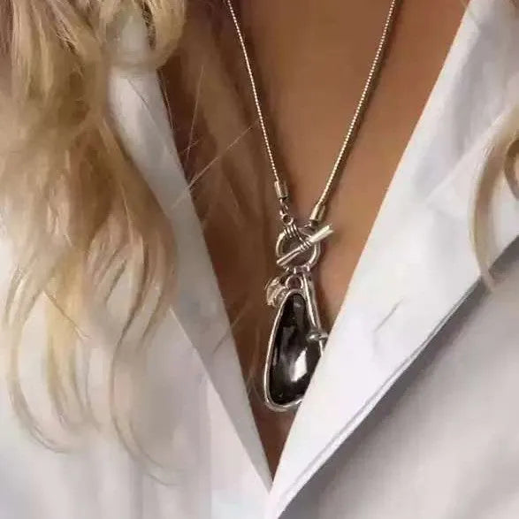 Geometric plaid pendant on a long snake chain necklace layered over a jumper.