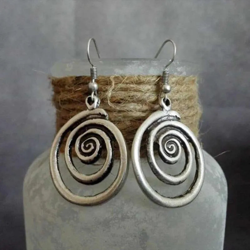 Close-up of a pair of silver geometric spiral earrings with a distressed vintage finish.