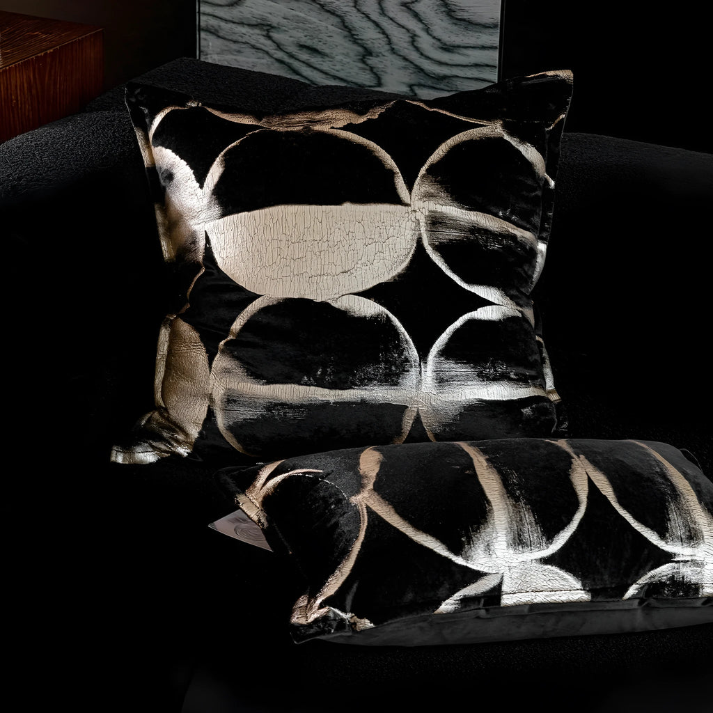 Black and gold abstract patterned flannel decorative cushion on a grey sofa.