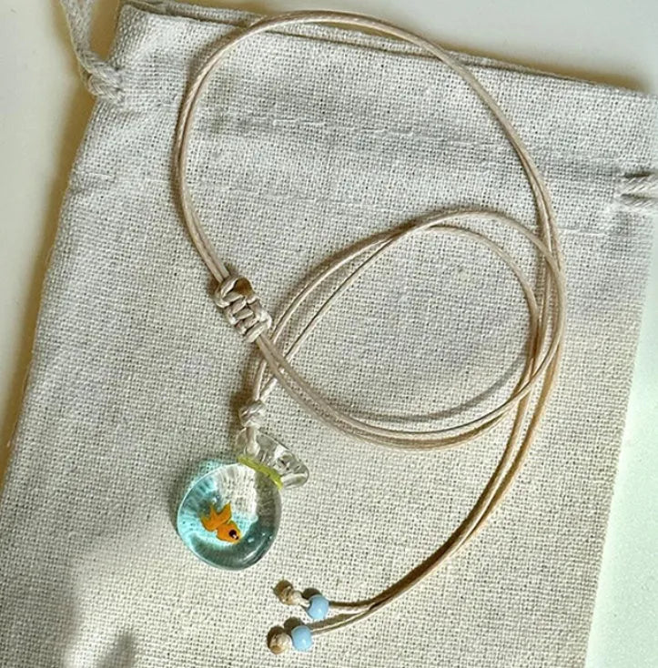 Women's necklace with blue glazed small fish charm pendant on a beige cotton-linen clavicle chain.