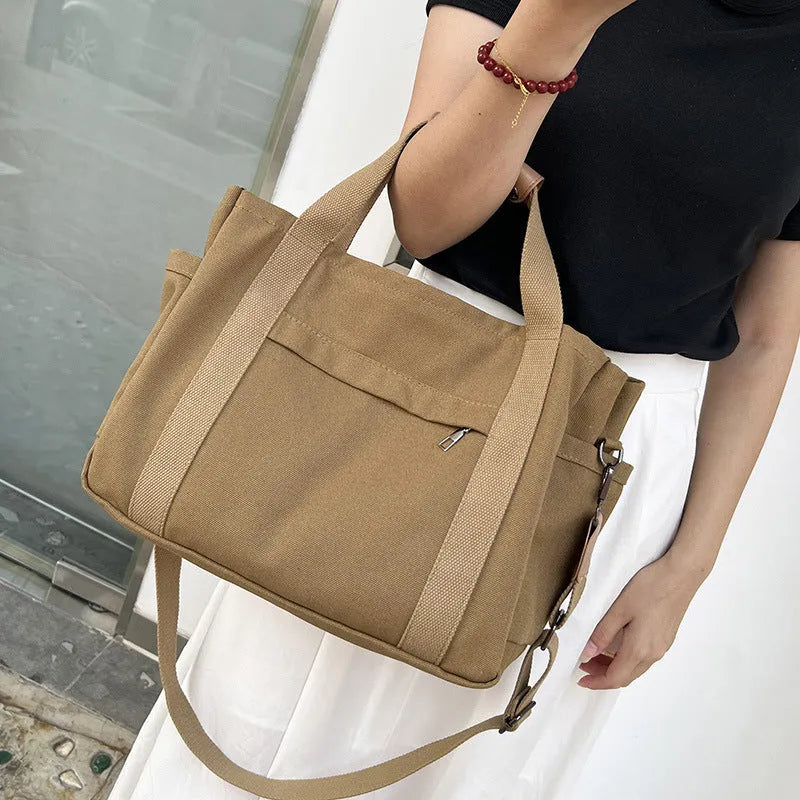 Army green canvas tote bag with open zip sides showing internal laptop and camera pockets.