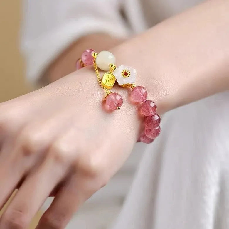 Handmade strawberry quartz crystal bracelet with peach blossom charms on a wrist.