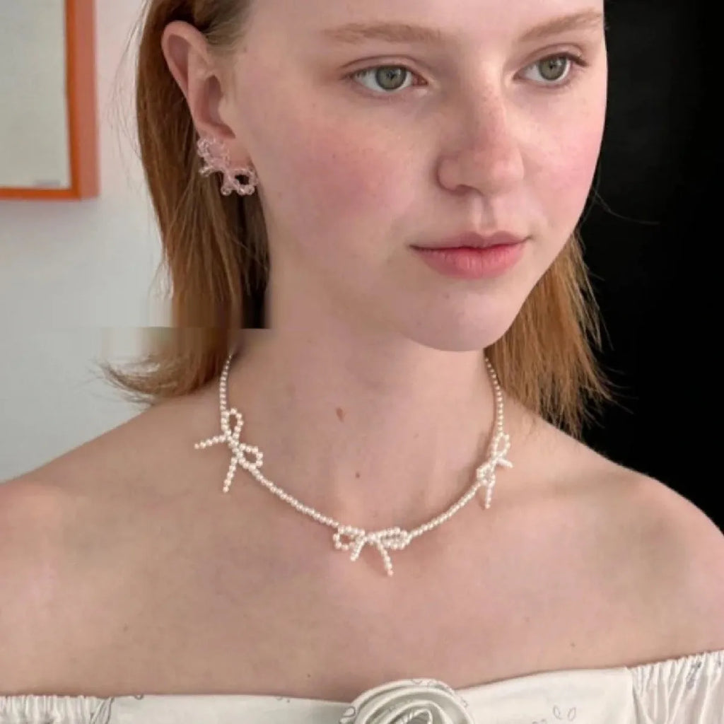 White imitation pearl necklace with a geometric bow charm on an adjustable chain.