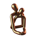 Modern minimalist loving couple resin statue in milky white or gold finish on a desk.