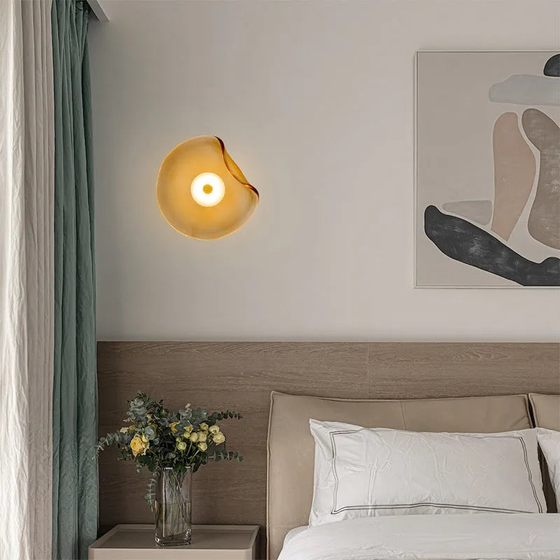 Round glass wall lamp in cognac colour mounted beside bed with warm lighting