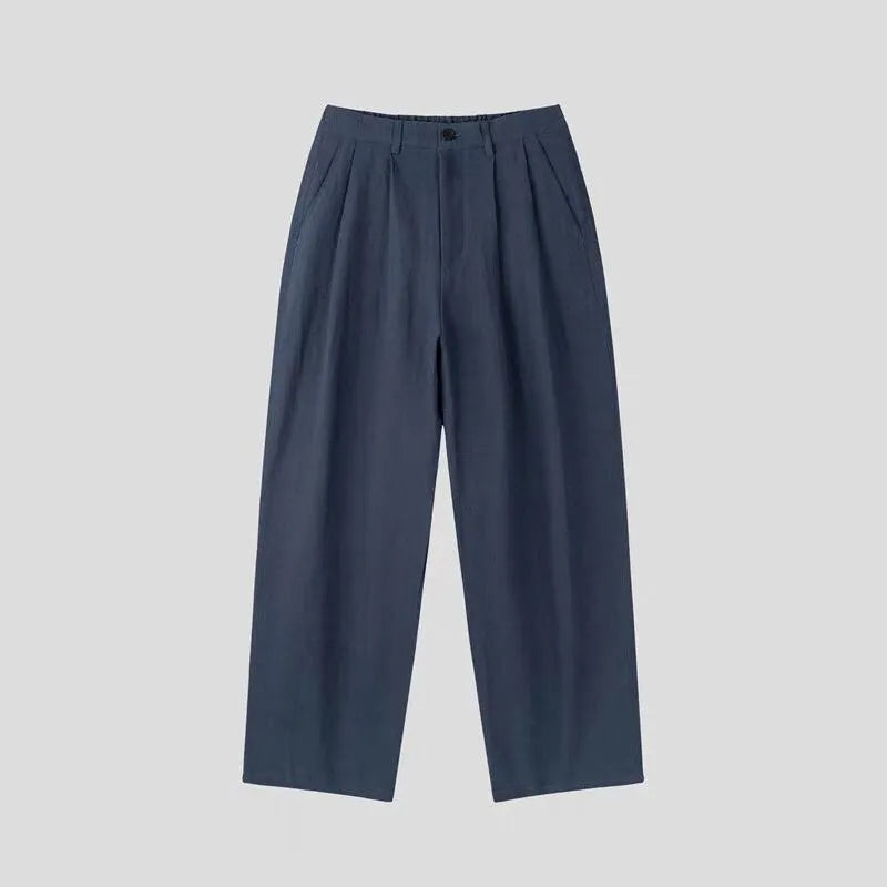 Men's apricot coloured loose-fit cotton linen trousers with a pencil leg and elastic waist on a neutral background.