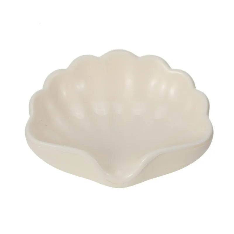 White shell-shaped plastic soap dish for bathroom counter next to pink version.