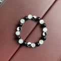 A polished black agate opal beaded bracelet with an ornamental Tai Chi symbol, shown on a wrist.