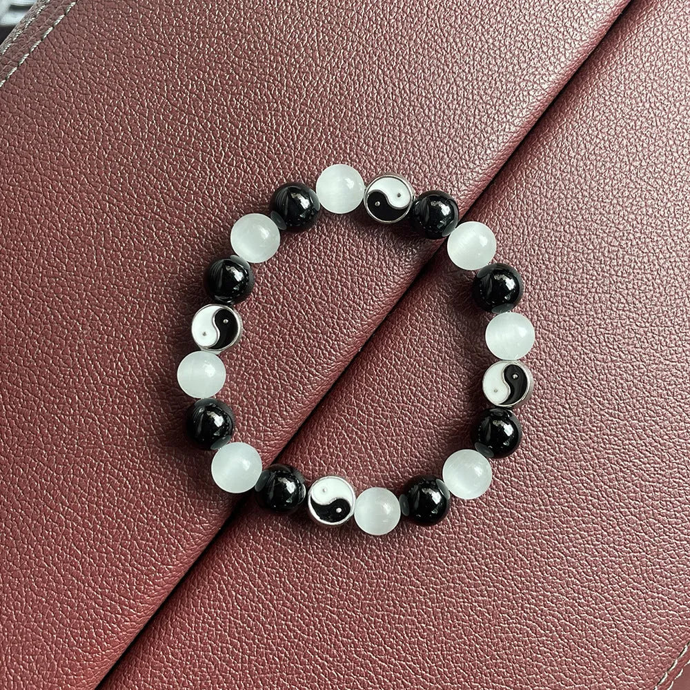 A polished black agate opal beaded bracelet with an ornamental Tai Chi symbol, shown on a wrist.
