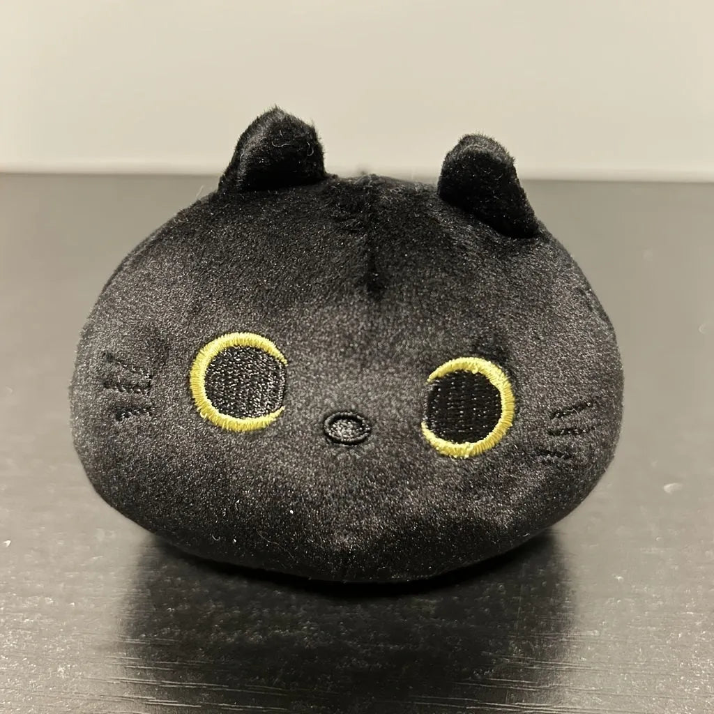 Fluffy black cat plush toy with embroidered face on a soft cushion