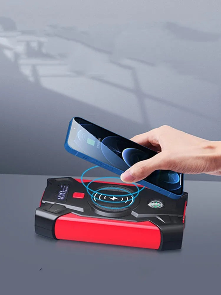 Red portable car jump starter and power bank unit with jumper cables on a table