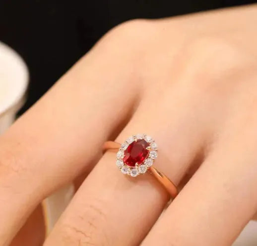 Women's silver ring with gold pigeon and red gemstone floral inlay on a finger.