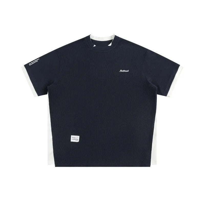 Man modelling a loose-fit navy blue waffle knit t-shirt with retro-style white alphabet embroidery on the front.