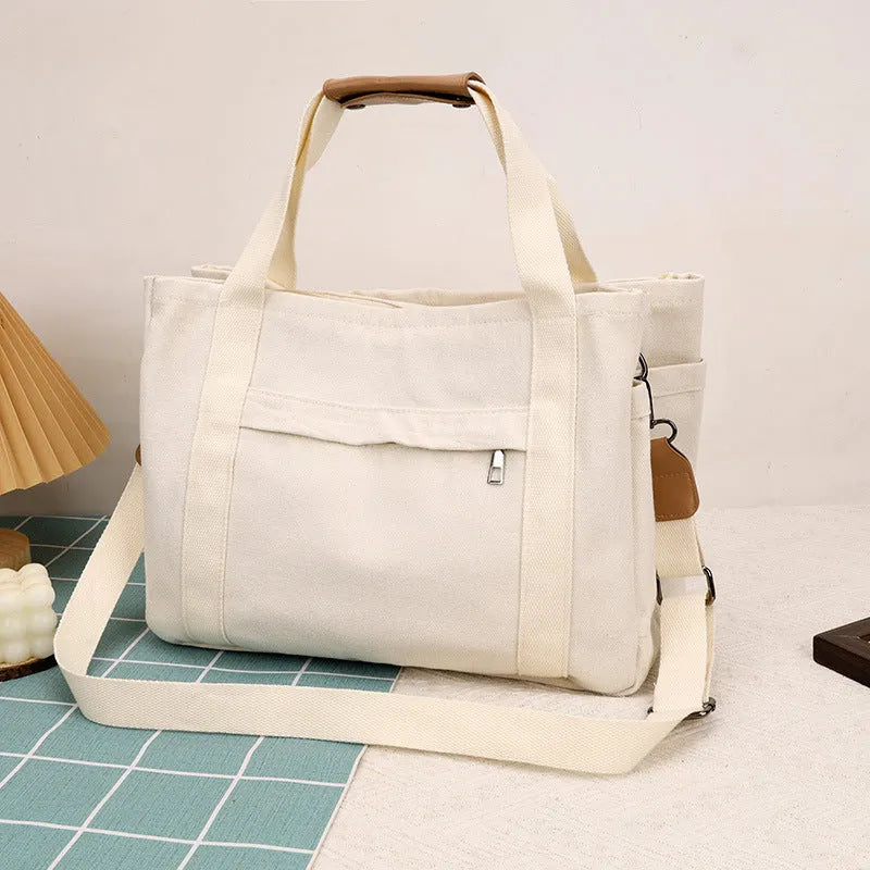 Army green canvas tote bag with open zip sides showing internal laptop and camera pockets.