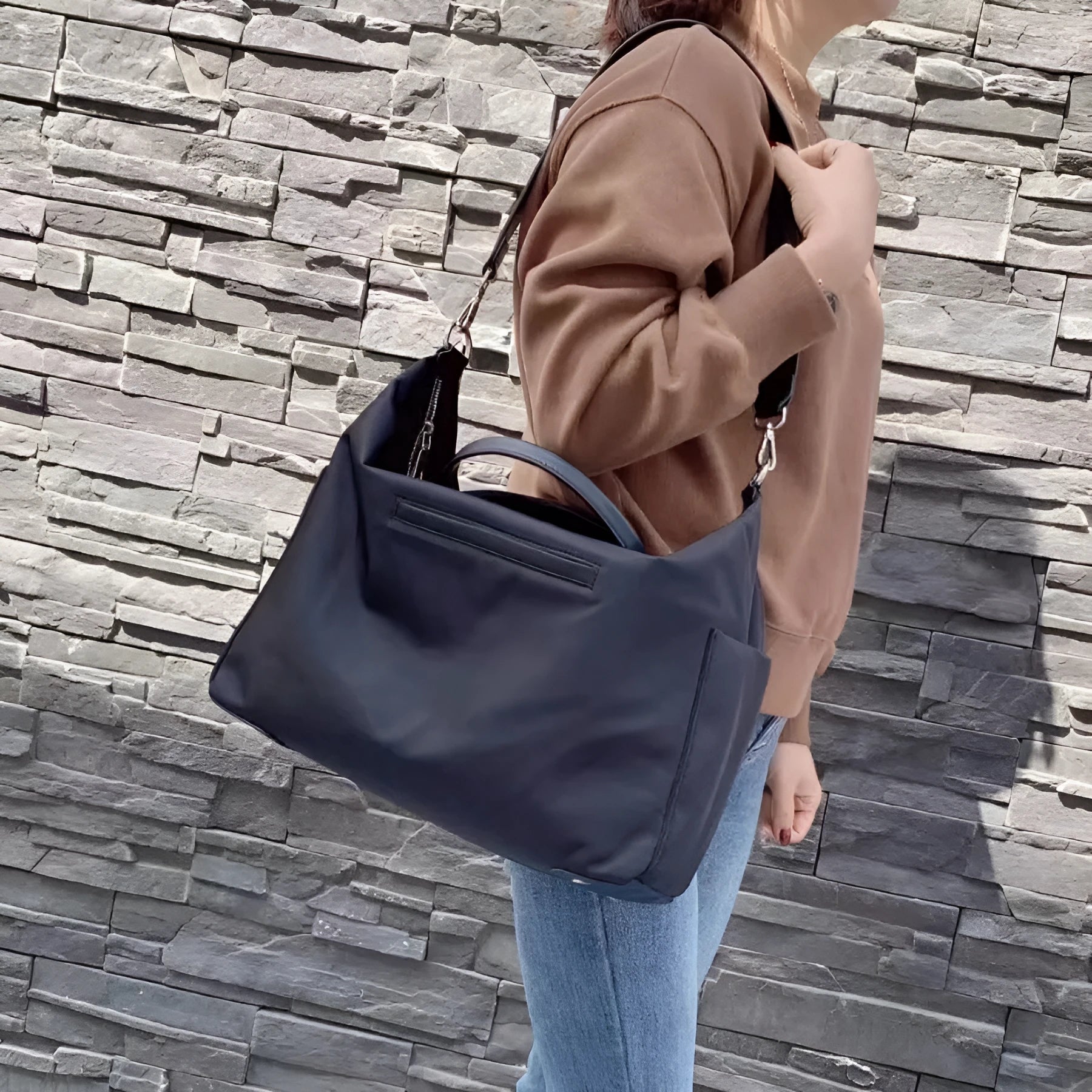 Black nylon waterproof shoulder bag with leather trim, showing large main compartment and shoulder strap.