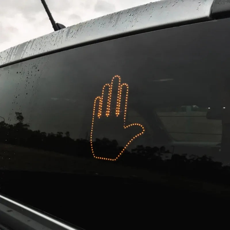 Black plastic LED car gesture light showing illuminated middle finger sign on dashboard