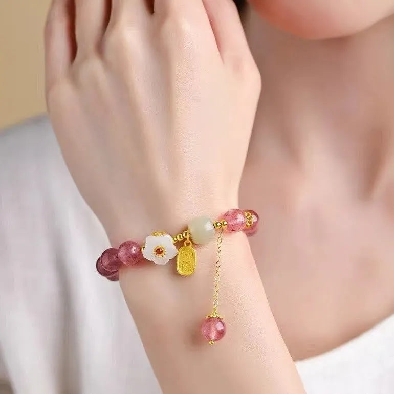Handmade strawberry quartz crystal bracelet with peach blossom charms on a wrist.