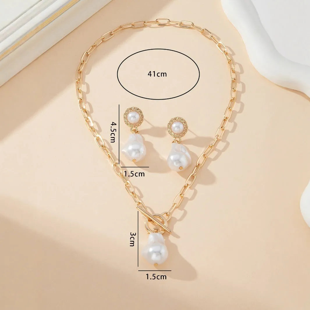 Gold baroque pearl pendant necklace and ear stud set for women on a white background.