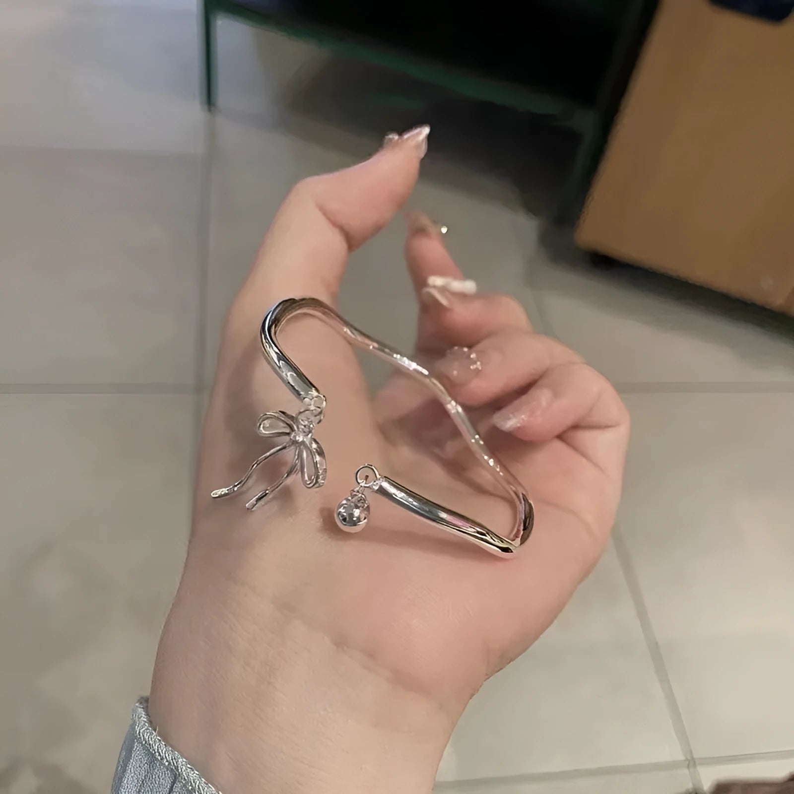 Silver adjustable women's bracelet with a bow bell charm on a zinc alloy bangle.