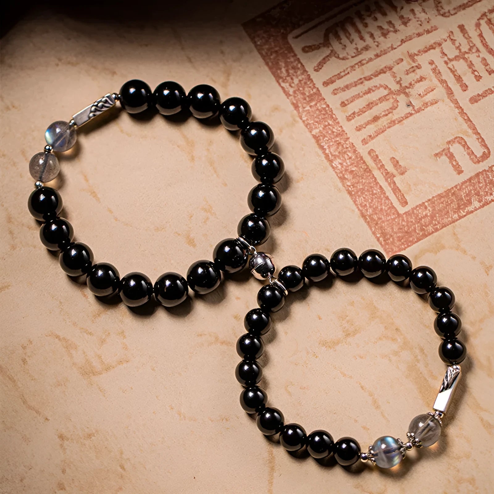 Black obsidian Buddha beads bracelets for couples, showing 8mm and 10mm bead sizes on a traditional cord.