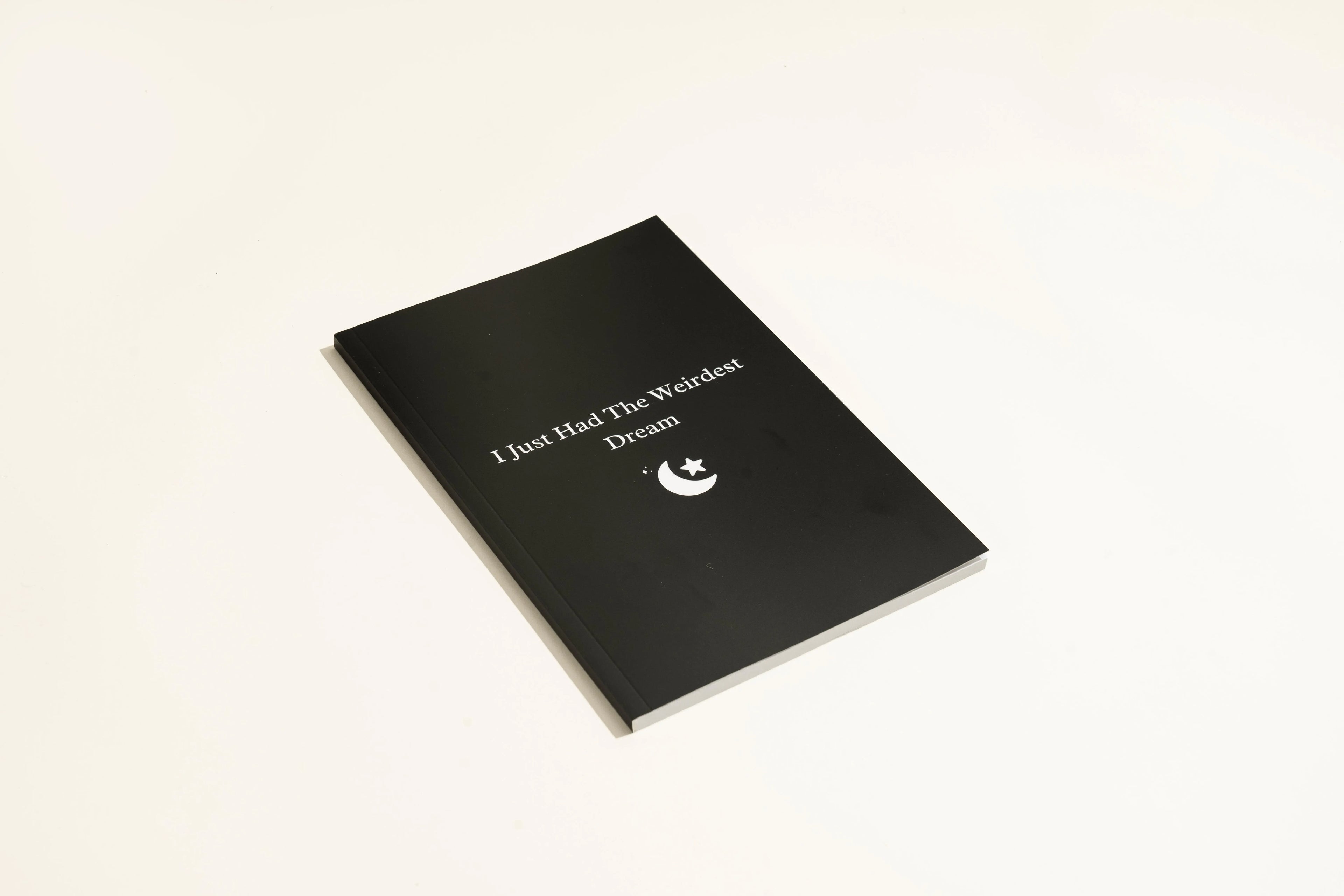 Black hardcover A5 dream journal notebook with plain pages, shown closed and open.