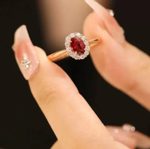 Women's silver ring with gold pigeon and red gemstone floral inlay on a finger.