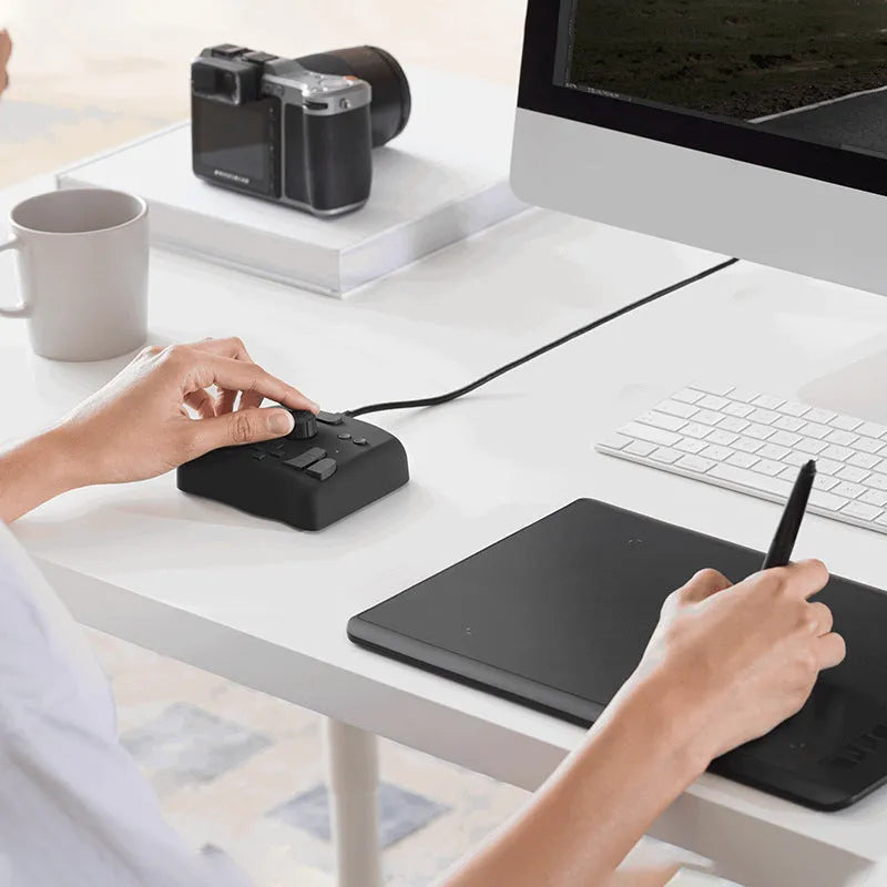 TourBox NEO black USB auxiliary keyboard for video editing on a desk, showing dials and buttons.