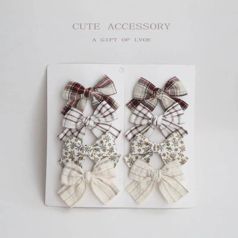 Set of eight children's cloth bow hairclips in assorted colours including beige, blue flowers, and polka dots.