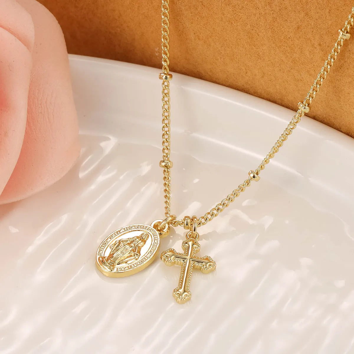 Gold-coloured geometric cross pendant necklace with a Virgin Mary ornament, on a chain.