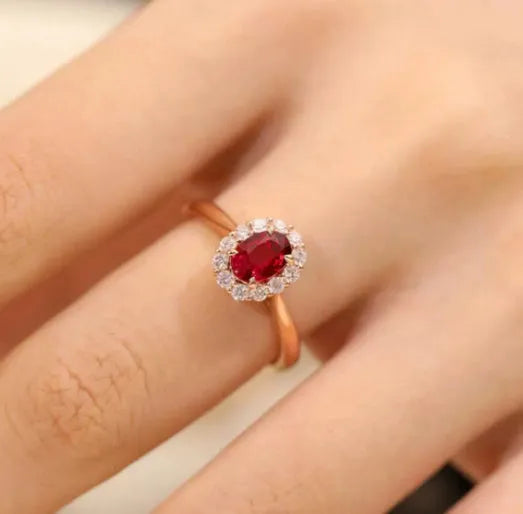 Women's silver ring with gold pigeon and red gemstone floral inlay on a finger.