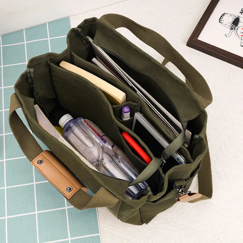 Army green canvas tote bag with open zip sides showing internal laptop and camera pockets.
