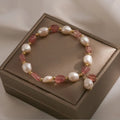 Handmade strawberry quartz crystal bracelet with peach blossom charms on a wrist.