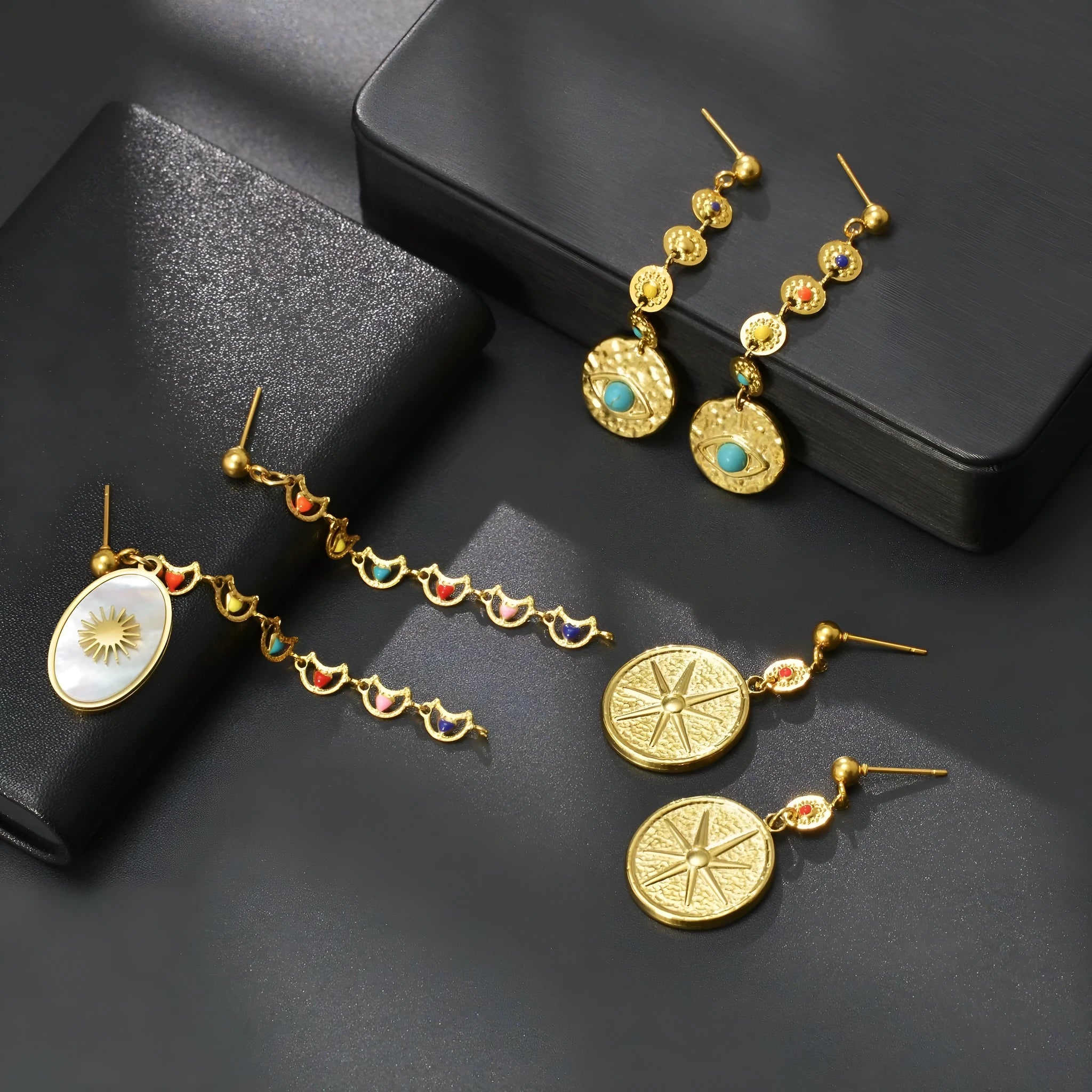 Geometric stainless steel stud earrings showing three colour options: Eight Awn XINGX, Eye, and Shell Sun designs.