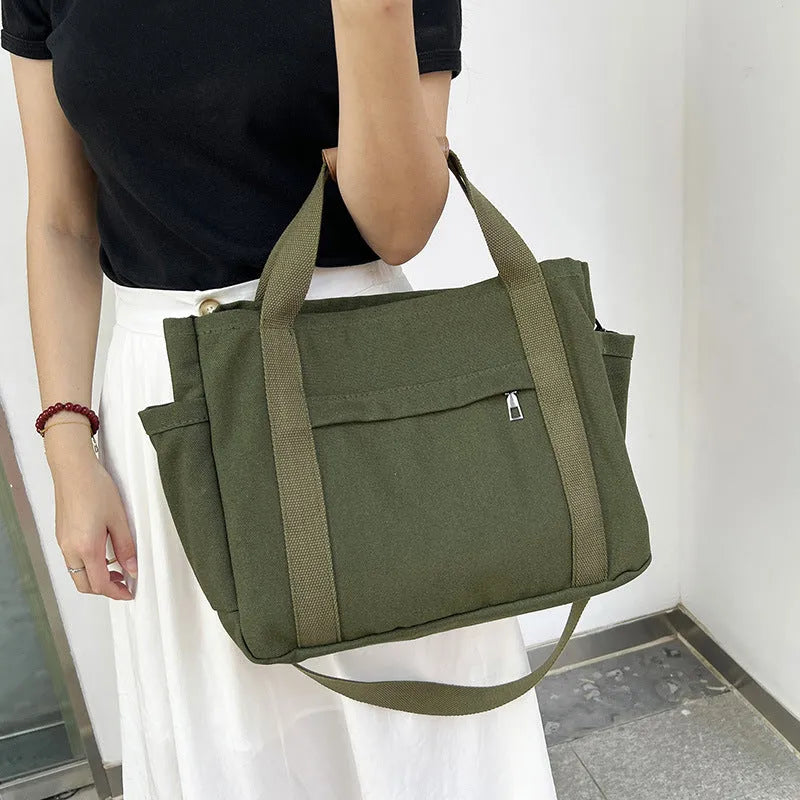 Army green canvas tote bag with open zip sides showing internal laptop and camera pockets.