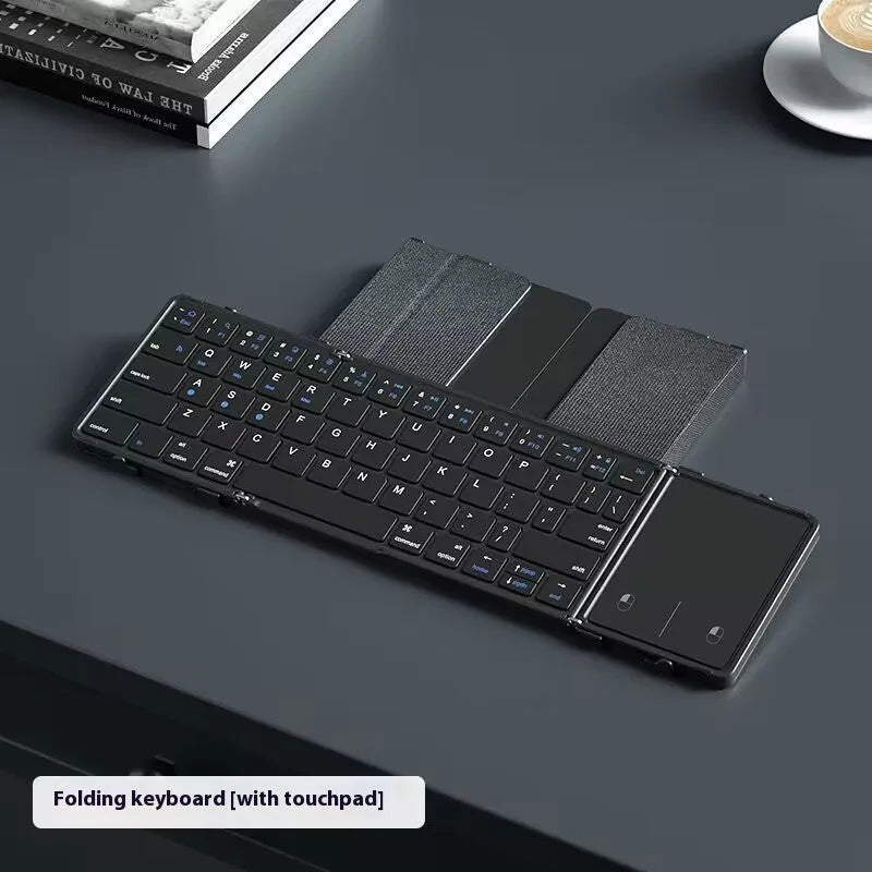 Black folding Bluetooth keyboard with touchpad unfolded next to mobile phone