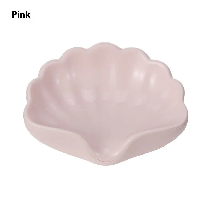 White shell-shaped plastic soap dish for bathroom counter next to pink version.