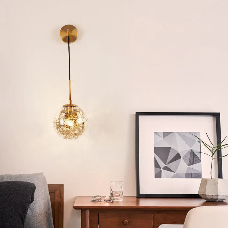 Modern glass wall lamp in golden flower finish mounted beside a bed.