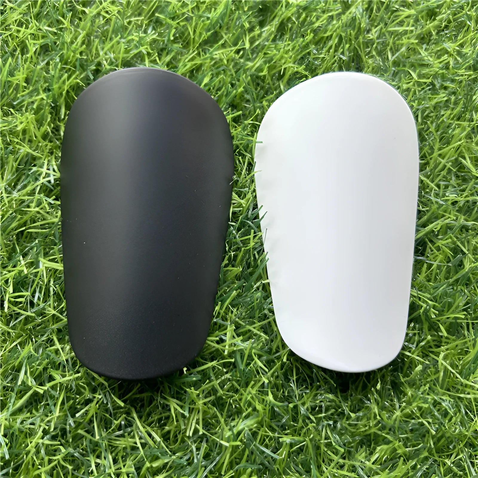 A pair of extra small mini plastic football shin guards, shown in either black or white.