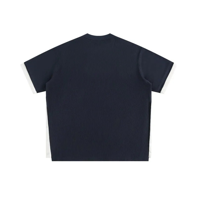 Man modelling a loose-fit navy blue waffle knit t-shirt with retro-style white alphabet embroidery on the front.