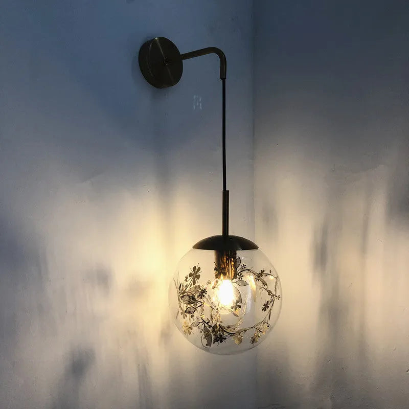 Modern glass wall lamp in golden flower finish mounted beside a bed.