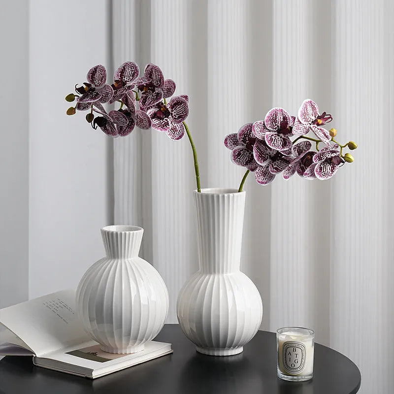 White ceramic ball vase with vertical stripes on a wooden table, with optional artificial purple orchid stems.