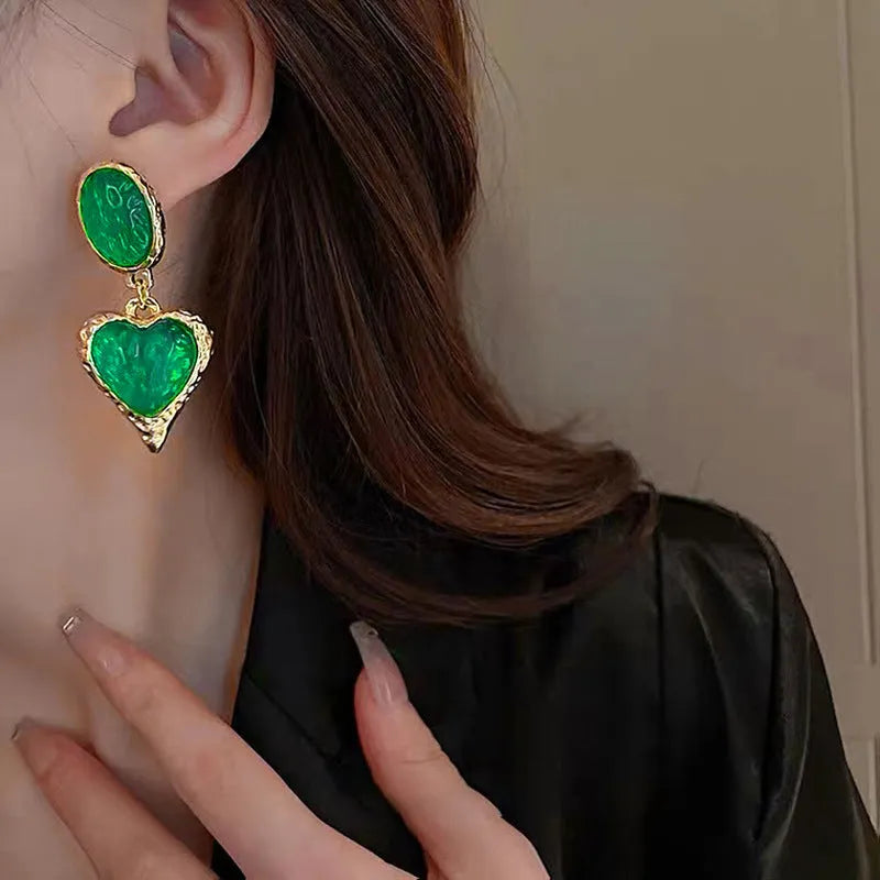 A pair of oval-shaped love heart stud earrings with a pleated surface, shown in one of four colour options.
