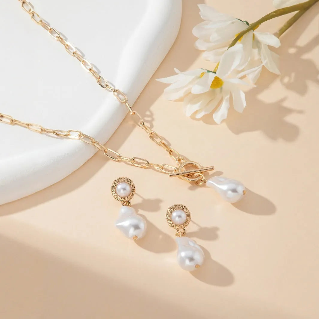 Gold baroque pearl pendant necklace and ear stud set for women on a white background.