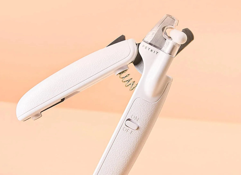 White pet nail clippers with LED light and transparent splash guard open, showing the triangular steel blade.
