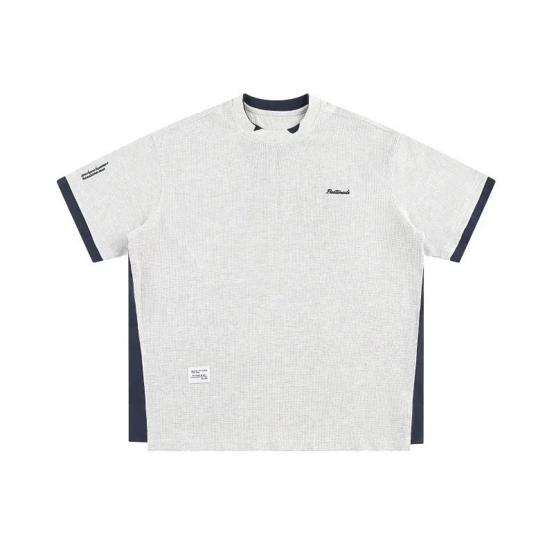 Man modelling a loose-fit navy blue waffle knit t-shirt with retro-style white alphabet embroidery on the front.