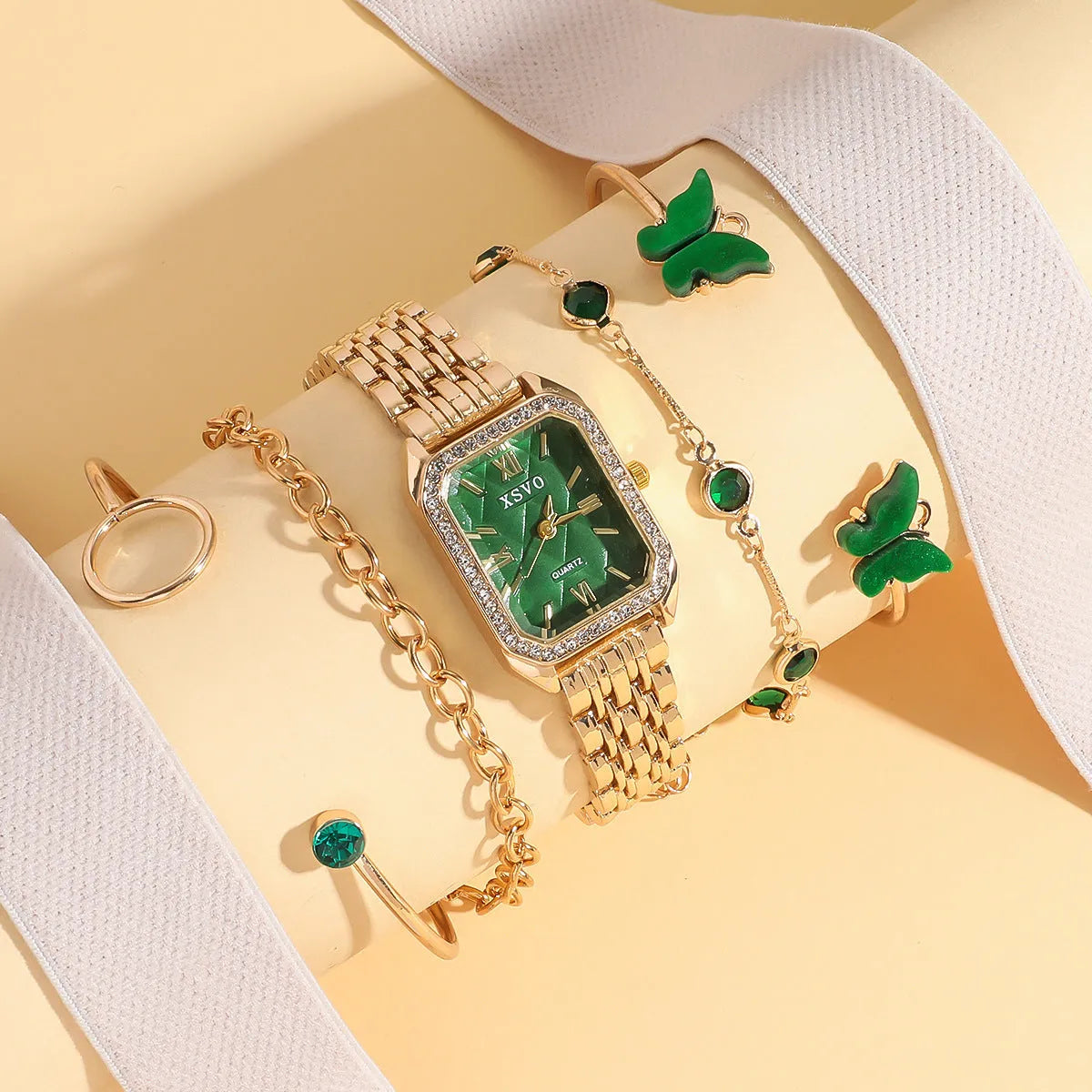 Gold green square steel ladies watch and four matching butterfly jewellery bracelets laid out as a set.